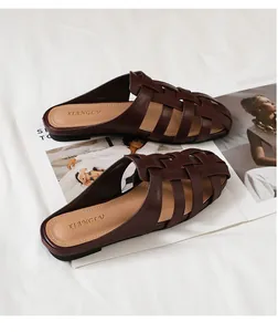 Primer plano de mules trenzados marrones con diseño calado sobre fondo de tela blanca suave