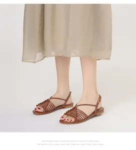 Primer plano de sandalias planas marrones con tiras trenzadas y hebilla en modelo