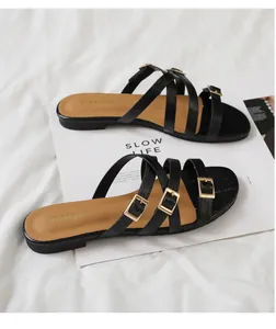 Close-up of black flat sandals with triple cross straps and gold metal buckles on a magazine