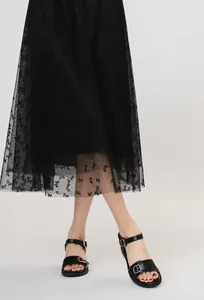 Dettaglio di sandali neri con zeppa e fibbie in metallo dorato con gonna in tulle
