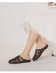 Detail of dark brown woven leather mule with golden buckle on a white dress background