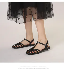 Detail von schwarzen flachen geflochtenen Sandalen mit T-Riemen und Metallschnalle