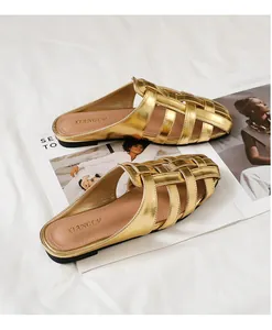 Detalle de mules planos dorados trenzados con diseño cruzado metálico en tela blanca