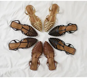 Flat woven gladiator sandals in gold, brown, and black displayed on white fabric