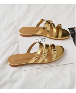 Detail of gold metallic flat sandals with multi-strap buckle design on a white magazine