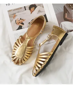 Detalle de sandalias romanas doradas con tiras en T, acabado metálico y hebilla tobillera
