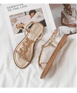 Detail of champagne gold flat sandals featuring rhinestone butterfly charms on T-strap