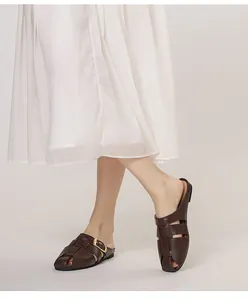 Close-up of brown woven leather mule with gold buckle paired with white skirt