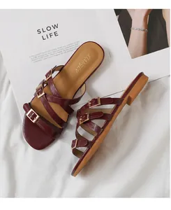 Detail of dark red strappy flat sandals with golden buckles on a white fabric surface