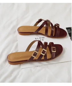 Detail showing dark red faux animal skin straps and gold buckles on flat sandals