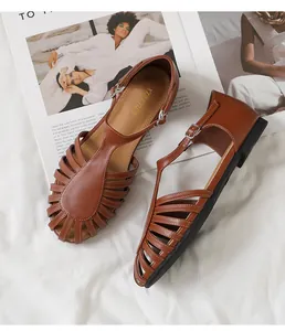 Primer plano de sandalias romanas planas marrones con diseño trenzado en T y hebilla metal
