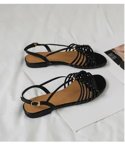 Detalle de sandalias planas negras con tiras cruzadas y hebilla dorada de estilo retro