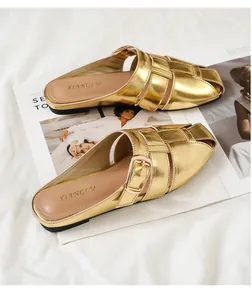 Detailed view of the metallic gold woven upper and gold buckle on a flat mule sandal