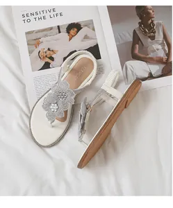 Detailed view of white flat sandals featuring rhinestone flowers and elastic heel strap
