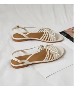 Detalle de sandalias planas trenzadas crema con tiras finas y hebilla metálica ajustable