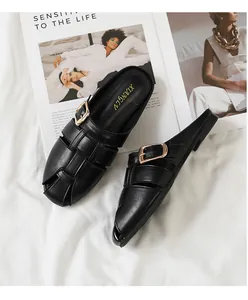 Detail of black leather woven mule featuring a golden buckle on a textured fabric