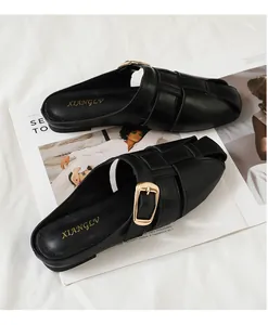Close-up of black leather woven mule flats with a large square gold metal buckle