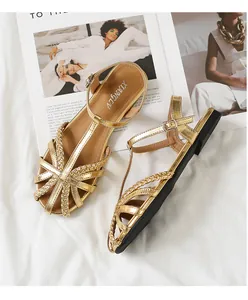 Detail von flachen geflochtenen Sandalen in Gold mit T-Riemen und Schnallenverschluss