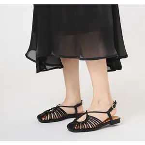 Detail of black woven strappy flat sandals featuring adjustable ankle buckle strap