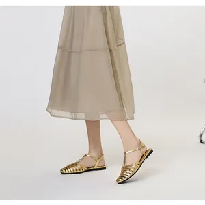 Detail of gold woven cutout flat sandals with buckle ankle straps on a model