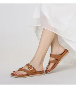 Vista lateral de sandalias marrones con hebilla dorada llevadas por modelo con vestido