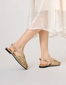 Detail of gold braided flat sandals with woven cutout straps and ankle buckle on a model