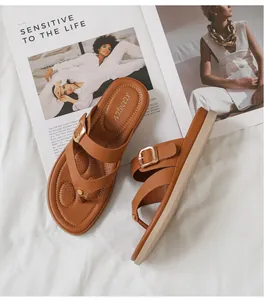 Detalle de sandalias de dedo en cuero sintético marrón con hebilla metálica sobre revista