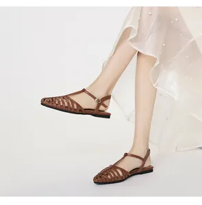 Detail of caramel brown woven leather flat sandals with ankle strap on a model's foot