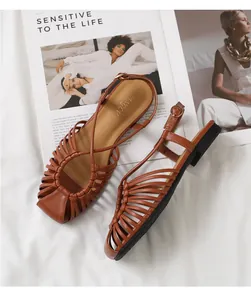 Detail of brown woven strap flat sandals with adjustable ankle buckle on white fabric