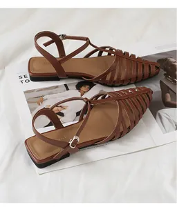Detail of woven caged leather flat sandals with adjustable ankle strap on a magazine