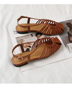 Close-up of caramel woven cutout flat sandals with adjustable ankle strap on white cloth