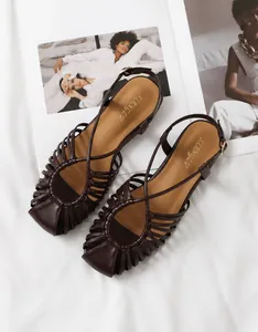 Close-up of dark brown woven cutout Roman sandals with gold ankle buckle on magazine