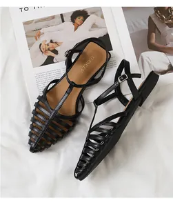Top view of black woven T-strap flat sandals with pointed toe on a lifestyle background