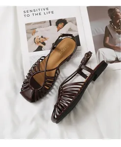 Detail of dark brown woven strappy sandals with buckle and gold branding on soft sole