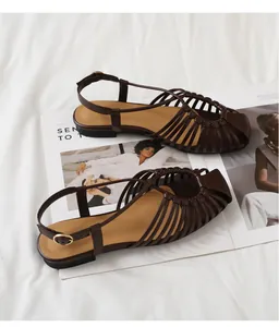 Close-up of brown hollow woven flat sandals with adjustable metal buckle on magazines