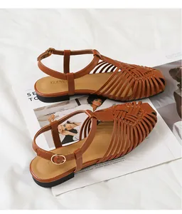 Dettaglio di sandali in pelle marrone intrecciata con cinturino a T e fibbia dorata