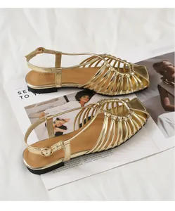 Flat gold woven sandals with square toe and ankle strap placed on a fashion magazine