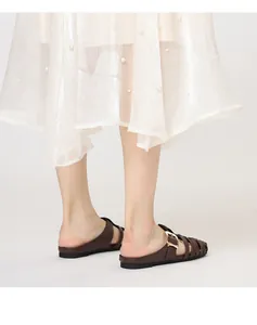 Detail of brown woven leather flat mule featuring a large golden buckle and mesh skirt