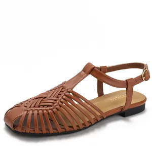 Sandali bassi in pelle marrone intrecciata con cinturino a T e fibbia dorata su bianco