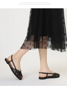 Detailansicht schwarzer geflochtener flacher Sandalen kombiniert mit einem Spitzenkleid