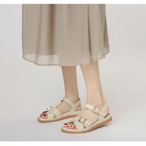 Dettaglio dei sandali romani beige piatti con cinturini incrociati e fibbia oro opaco