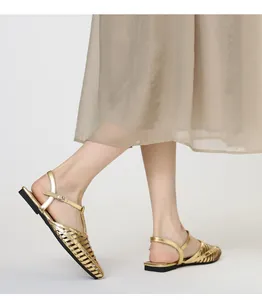 Makro-Detail von goldenen Metallic-Sandalen mit Nietendekor und geflochtenem Muster