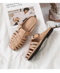 Detail of beige woven mules with leather straps and gold buckle on a stylish flat sole