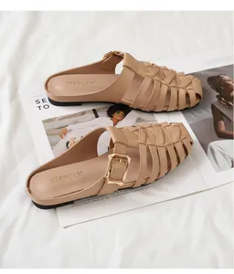 Close-up of woven hollow beige mule slippers with decorative gold buckle on a magazine