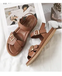 Dettaglio di sandali alla schiava in pelle marrone con fibbie in metallo dorato e suole piatte