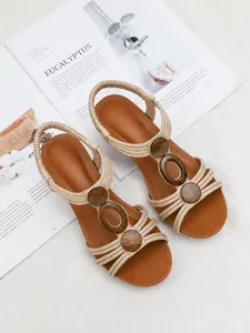 Flat wedge sandals with beige straps and wood-texture oval ornaments on a lifestyle background