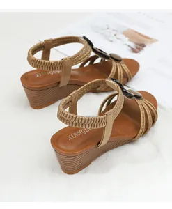 Detail of brown wedge sandals with leather straps and a decorative buckle on a wood sole