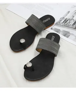 Détail de sandale plate noire avec anneau en strass étincelant et bride grise souple