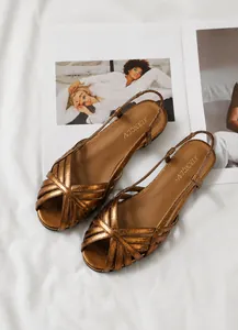 Detailansicht der bronzefarbenen Riemchensandalen auf einem Modemagazin und weißem Stoff