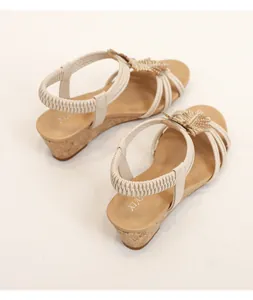Close-up of beige wedge sandals featuring woven leaf motifs and cork-textured platform heels